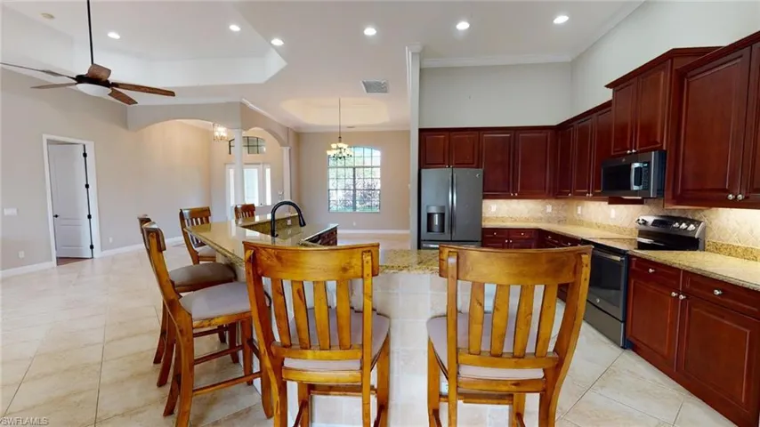 Kitchen featuring ceiling fan with notable chandelier, tasteful backsplash, light stone counters, appliances with stainless steel finishes, and light tile patterned flooring
