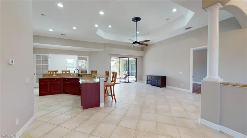 Kitchen with ceiling fan, sink, light stone countertops, and decorative columns