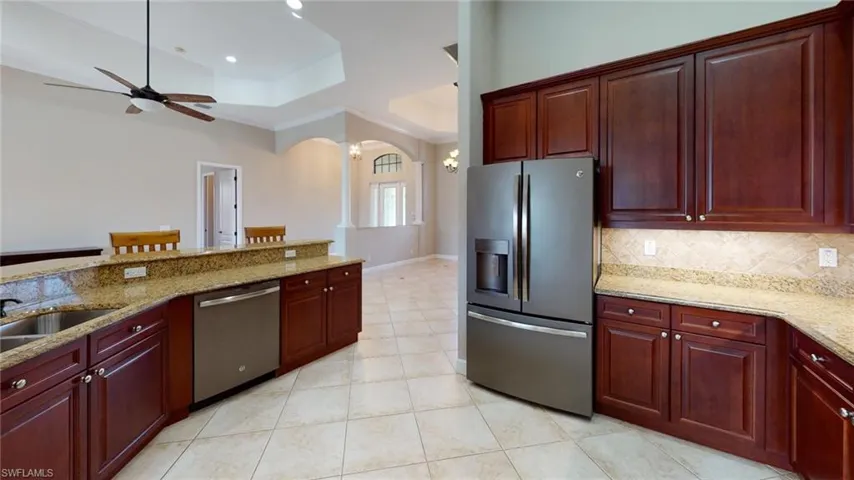 Kitchen featuring backsplash, light stone counters, stainless steel appliances, sink, and ceiling fan