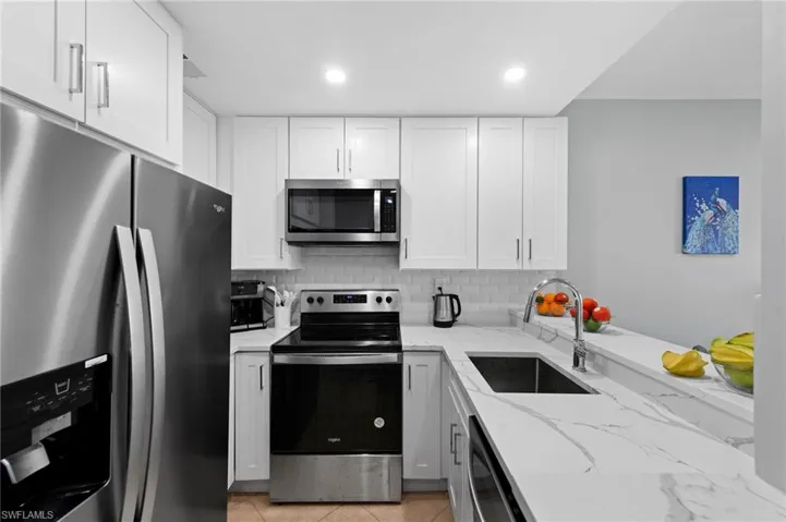 Kitchen featuring stainless steel appliances, light stone countertops, backsplash, white cabinets, and recessed lighting