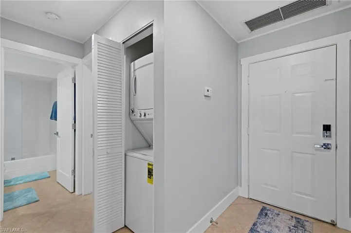 Laundry area featuring light tile patterned floors and stacked washing machine and dryer