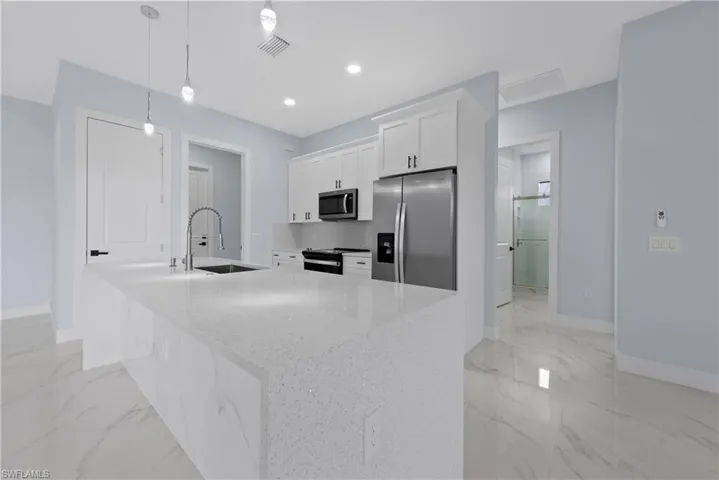 Kitchen with an island with sink, hanging light fixtures, sink, white cabinetry, and appliances with stainless steel finishes