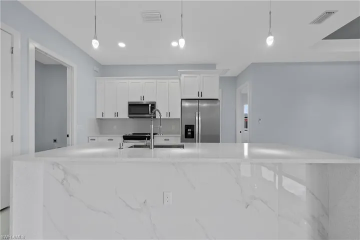Kitchen with light stone countertops, a kitchen island with sink, decorative light fixtures, and appliances with stainless steel finishes