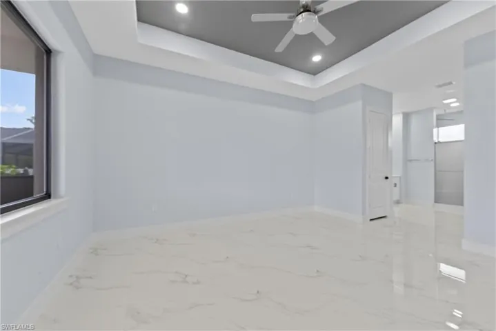 Spare room featuring ceiling fan, a tray ceiling, and light tile flooring