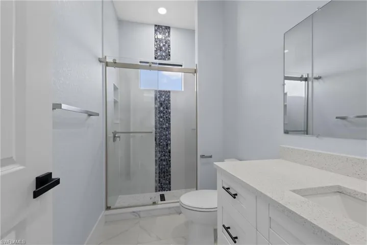 Bathroom featuring tile floors, a shower with door, toilet, and vanity