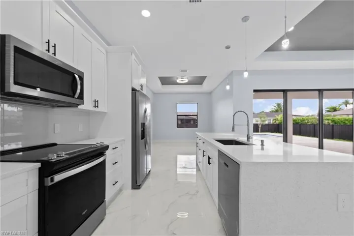 Kitchen with stainless steel appliances, an island with sink, sink, light tile flooring, and a raised ceiling