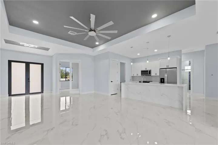 Unfurnished living room featuring ceiling fan, a tray ceiling, and light tile floors