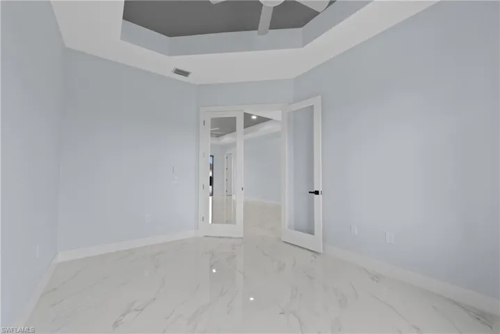 Tiled empty room with ceiling fan and a raised ceiling