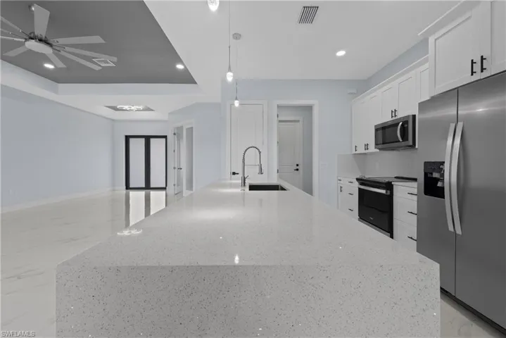 Kitchen featuring ceiling fan, a tray ceiling, stainless steel appliances, sink, and a kitchen island with sink