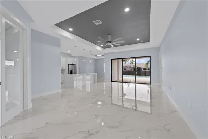 Empty room with ceiling fan, a tray ceiling, and light tile floors