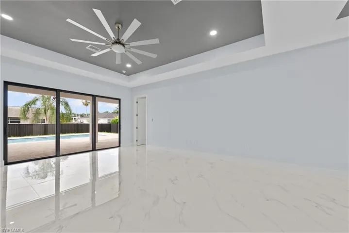 Tiled empty room with ceiling fan and a tray ceiling