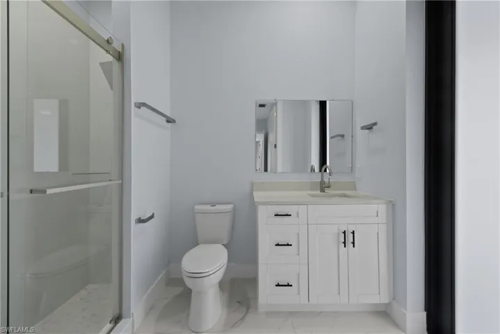 Bathroom featuring tile floors, a shower with door, toilet, and vanity