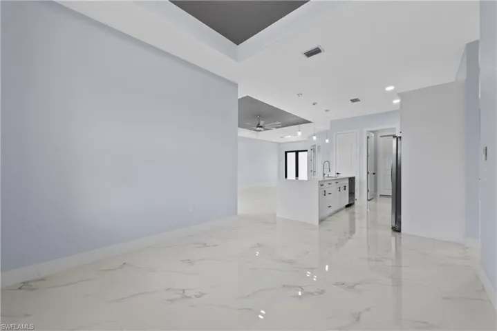 Empty room with a tray ceiling, sink, ceiling fan, and light tile floors