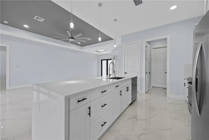 Kitchen featuring ceiling fan, a tray ceiling, a kitchen island with sink, white cabinets, and sink
