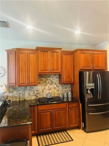 Kitchen with tasteful backsplash, stainless steel fridge, black gas stovetop, light tile patterned floors, and dark stone countertops