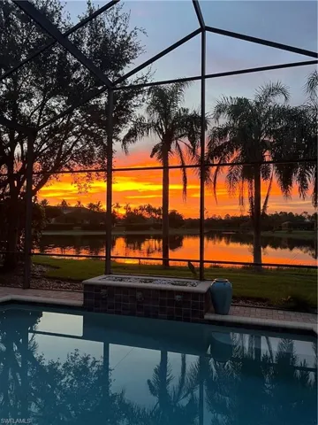 Pool at dusk featuring a water view and glass enclosure