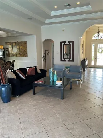 Living room with light tile patterned flooring, a tray ceiling, crown molding, and a notable chandelier