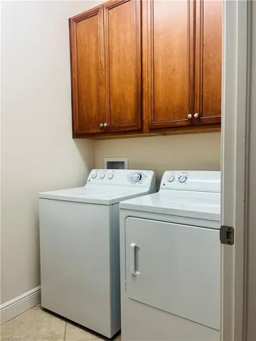 Clothes washing area with cabinets, washer and clothes dryer, and light tile patterned floors