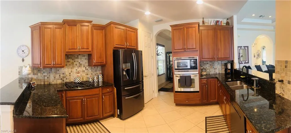 Kitchen featuring appliances with stainless steel finishes, light tile patterned floors, dark stone countertops, and tasteful backsplash