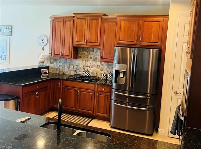 Kitchen with dark stone countertops, black gas stovetop, light tile patterned floors, and stainless steel refrigerator with ice dispenser