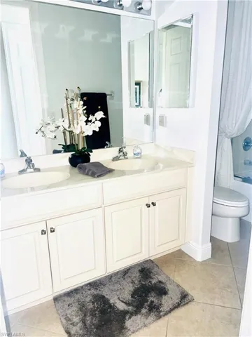 Full bathroom with shower / bathtub combination, dual vanity, toilet, and tile patterned flooring