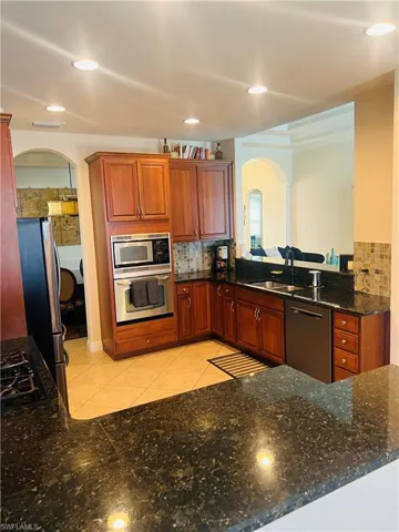 Kitchen with decorative backsplash, sink, dark stone countertops, appliances with stainless steel finishes, and light tile patterned floors
