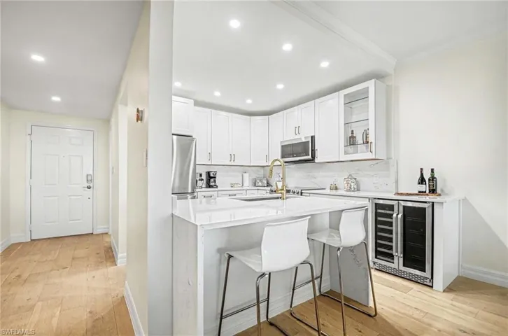 Kitchen featuring a breakfast bar, light stone counters, wine cooler, white cabinetry, and light wood-type flooring