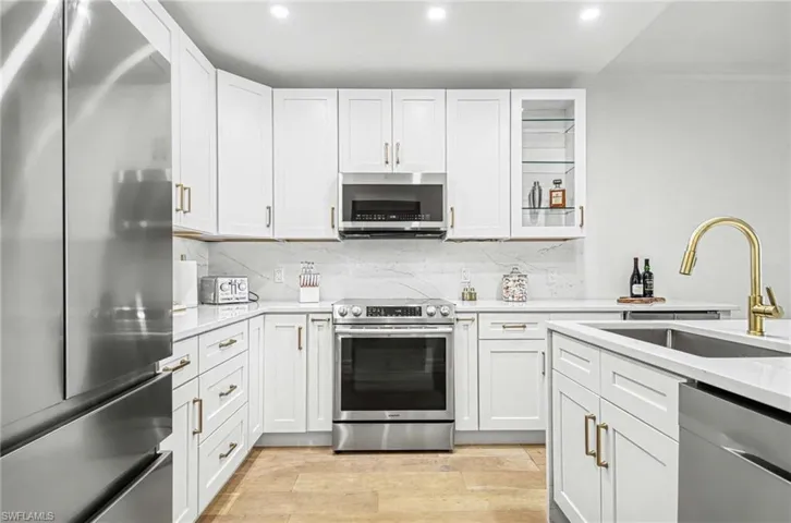 Kitchen featuring stainless steel appliances, white cabinets, light stone counters, light wood-style flooring, and recessed lighting