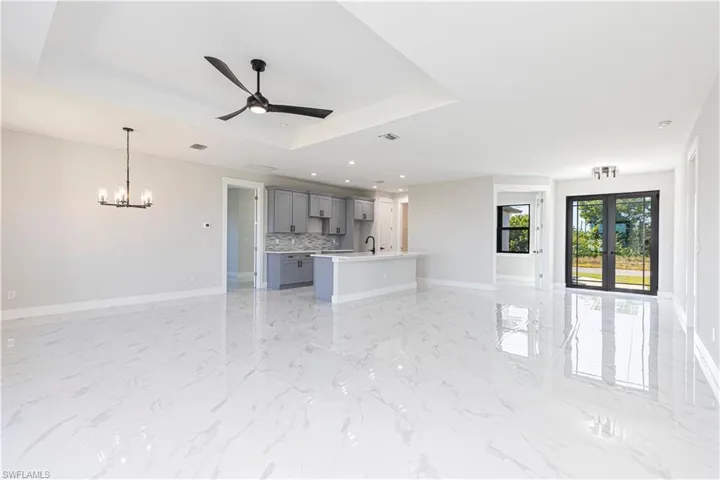 Unfurnished living room featuring ceiling fan, french doors, a tray ceiling, a chandelier, and light marble finish flooring