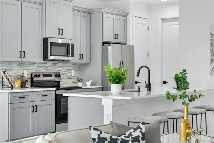 Kitchen featuring gray cabinets, stainless steel appliances, light stone counters, and a center island with sink