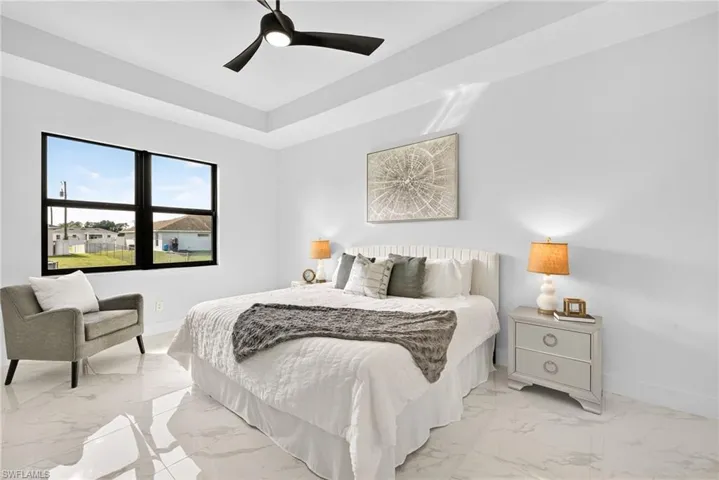 Bedroom with light marble finish floors, a ceiling fan, and a tray ceiling