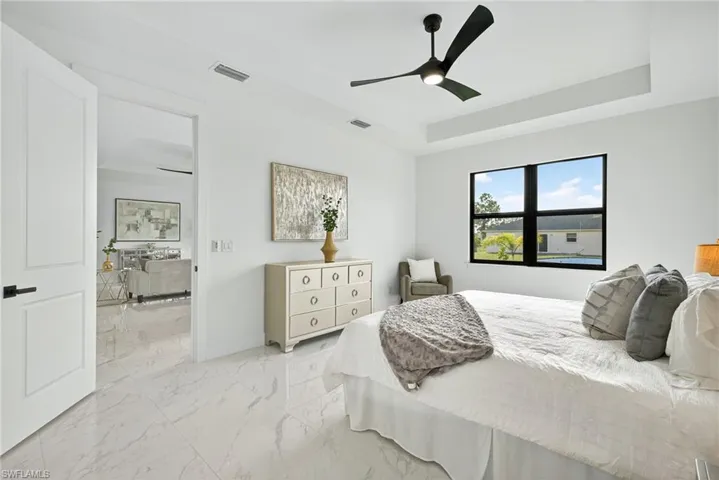 Bedroom with a raised ceiling, light marble finish floors, and ceiling fan