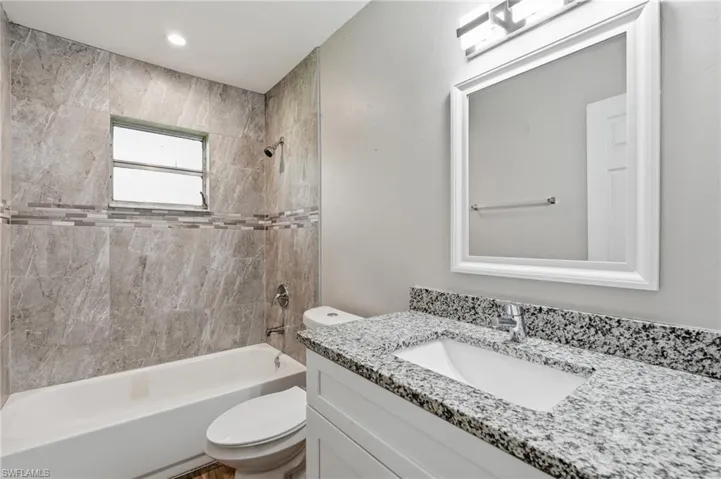 Bathroom featuring a white vanity with a speckled countertop, a framed mirror, a tiled shower surround with a decorative accent band, and a white bathtub