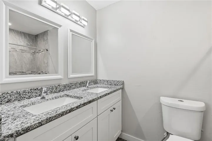 Dual vanity with undermount sinks, granite countertops, white cabinetry, and framed mirrors