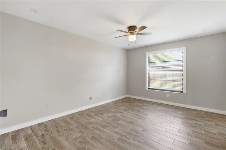 Wood-finish tile flooring, recessed ceiling lighting, a ceiling fan with integrated lighting, and a window with blinds