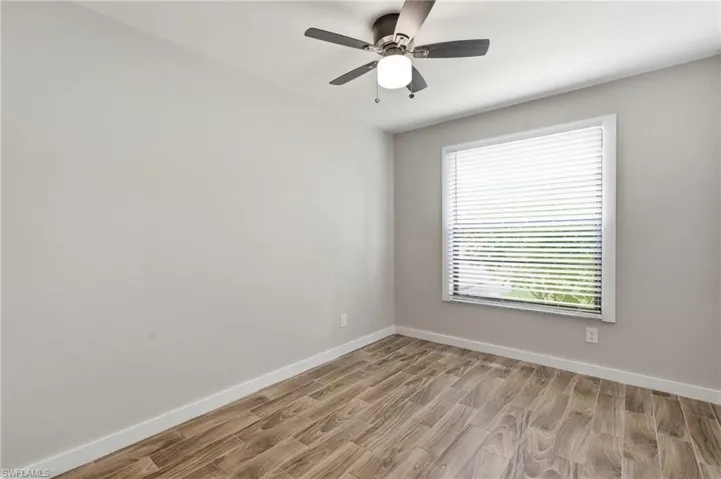 Wood-finish flooring, neutral wall tones, window with horizontal blinds, and a ceiling fan with integrated lighting