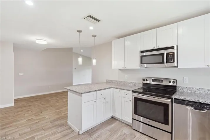 Kitchen featuring white shaker cabinetry, stainless steel appliances, speckled countertops, pendant lighting, and wood-finish flooring