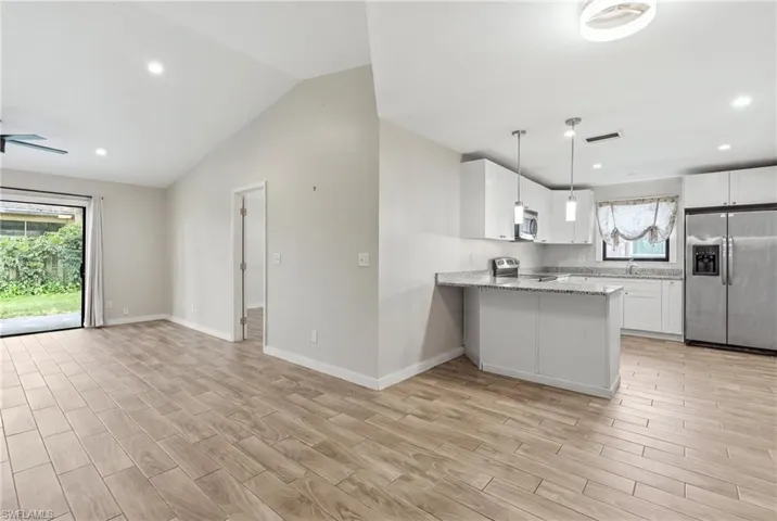 Open-concept kitchen and dining area featuring white cabinetry, stainless steel appliances, a center island with pendant lighting, wood-finish flooring throughout, and sliding glass doors opening to the outdoor space