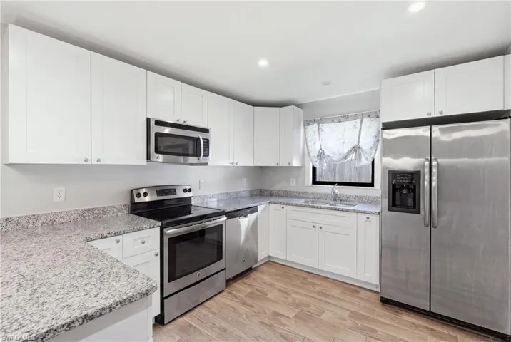 Modern kitchen featuring white cabinetry, stainless steel appliances, granite countertops, wood-finish flooring, and recessed lighting