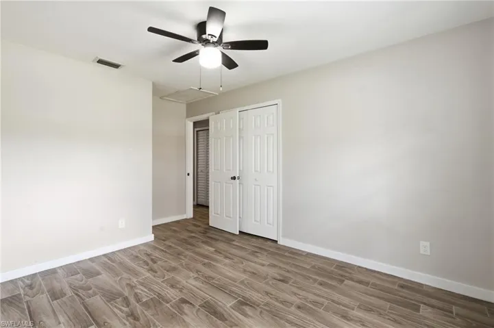 Wood-finish flooring, neutral wall tones, ceiling fan with integrated lighting, and white bi-fold closet doors