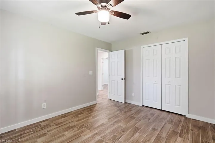 Wood-finish flooring, neutral wall tones, white bi-fold closet doors, white interior door, and a ceiling fan with integrated lighting