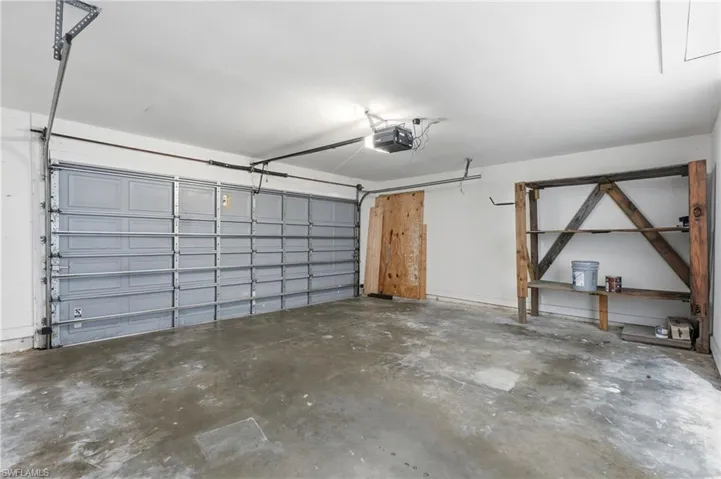 Spacious garage featuring a sectional overhead door, concrete flooring, ceiling-mounted storage infrastructure, and built-in wooden shelving unit with multiple display tiers