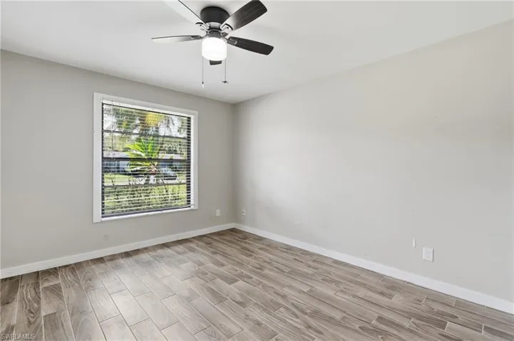 Neutral gray walls, wood-finish flooring, a window with horizontal blinds, and a ceiling fan with integrated lighting