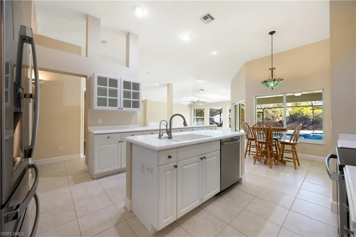 Kitchen with an island with sink, sink, white cabinets, light tile patterned flooring, and appliances with stainless steel finishes