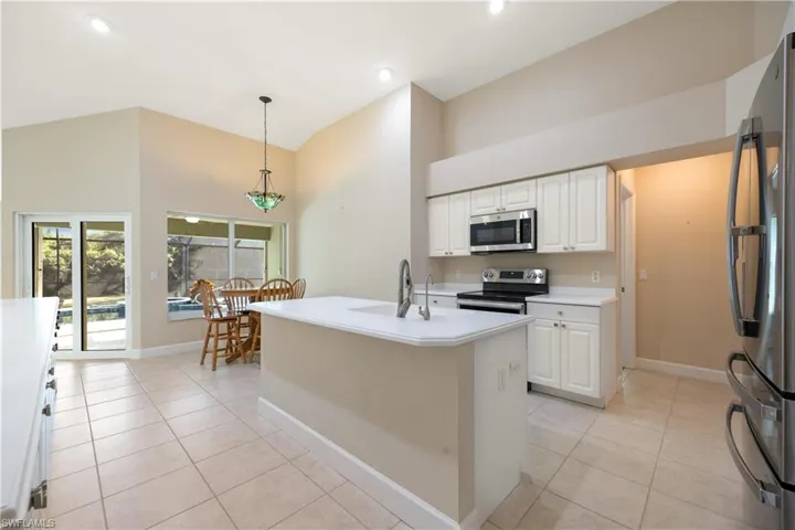Kitchen featuring appliances with stainless steel finishes, sink, an island with sink, hanging light fixtures, and white cabinets