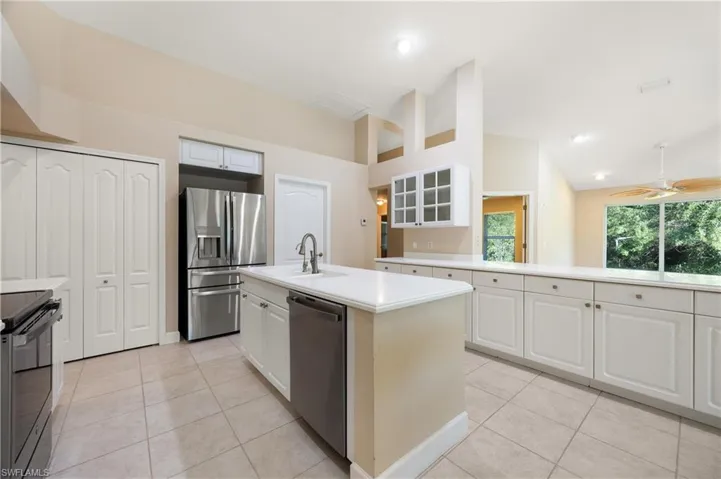 Kitchen featuring appliances with stainless steel finishes, white cabinets, a center island with sink, and vaulted ceiling