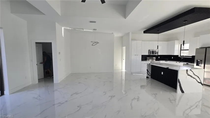 Kitchen with decorative light fixtures, white cabinets, a center island, stainless steel appliances, and light stone counters