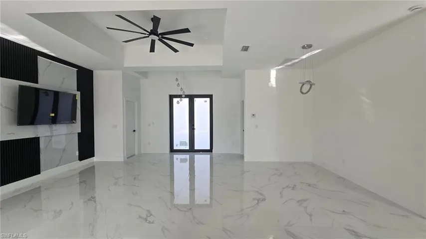 Unfurnished living room featuring light marble finish floors, french doors, a ceiling fan, and a tray ceiling