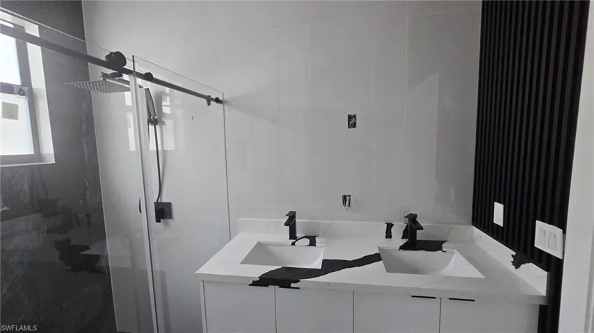 Full bathroom with double vanity and a marble finish shower
