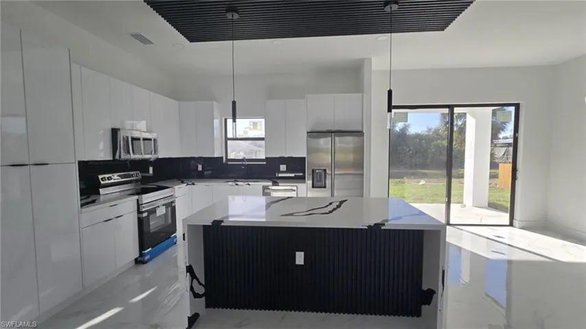 Kitchen with a kitchen island, stainless steel appliances, backsplash, light marble finish floors, and plenty of natural light